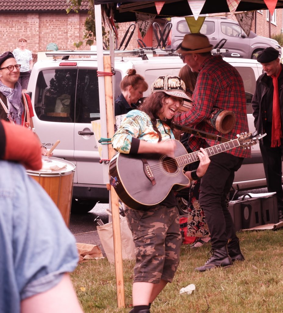 Women smiling and playing the guitar outside at Sylvania Community Store's grand opening event
